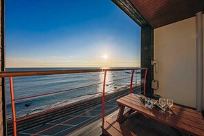A balcony with a wooden table, a railing, and a view of the ocean at sunset. - Sea Island Pension (Yeongdeok)