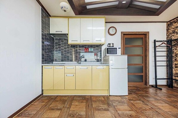 Una cocina compacta con armarios amarillos, un refrigerador blanco, un microondas y piso de madera.