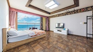 Une chambre avec un plancher en bois, un lit avec une literie blanche, une télévision et une vue sur la mer.