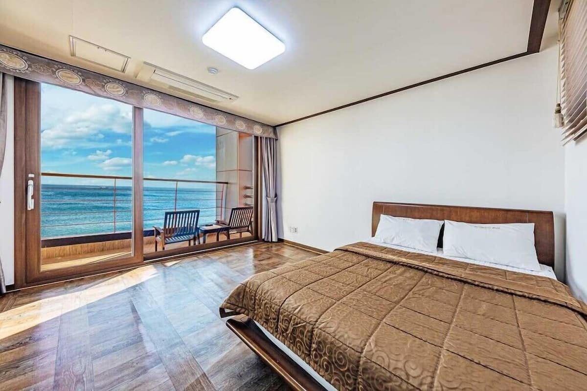 A bedroom with a large bed, a view of the ocean through a sliding glass door, and a balcony with a chair.