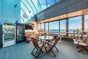 A modern lounge area with a round table and chairs, a television, and a vending machine. - Sea Island Pension (Yeongdeok)