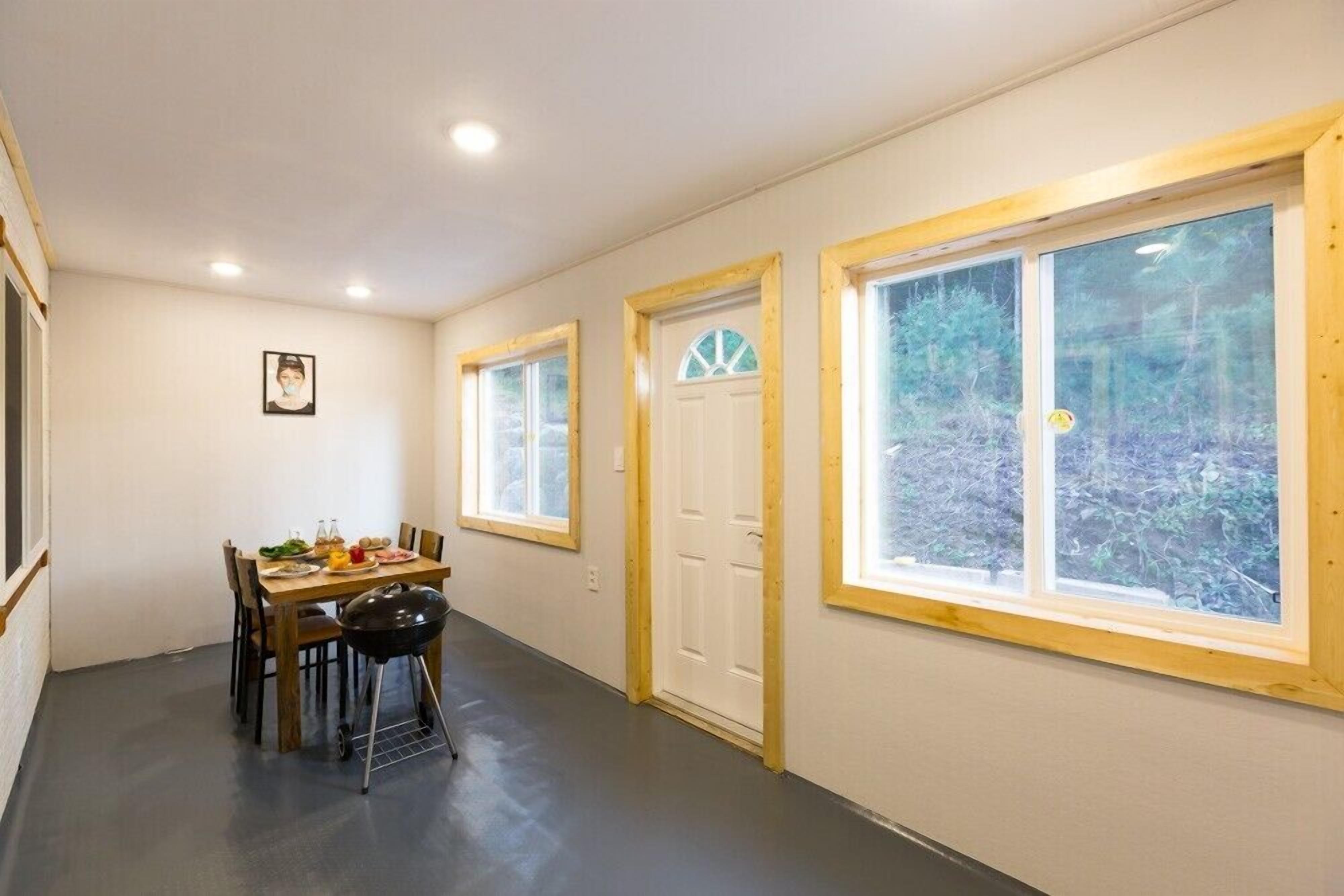 A dining area with a table set for four, a grill, and a view of the outdoors through large windows.