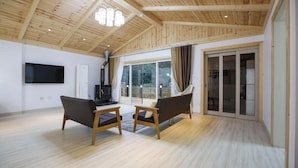 Amplia sala de estar con suelo de madera, televisor de pantalla plana, dos sofás y un gran ventanal corredero que da a un espacio exterior.