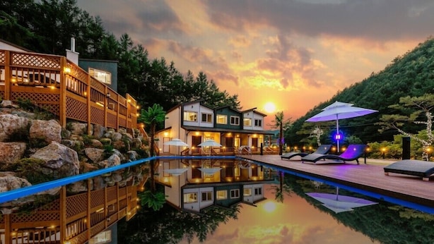 Una casa moderna con piscina, terraza de madera y vista al atardecer.