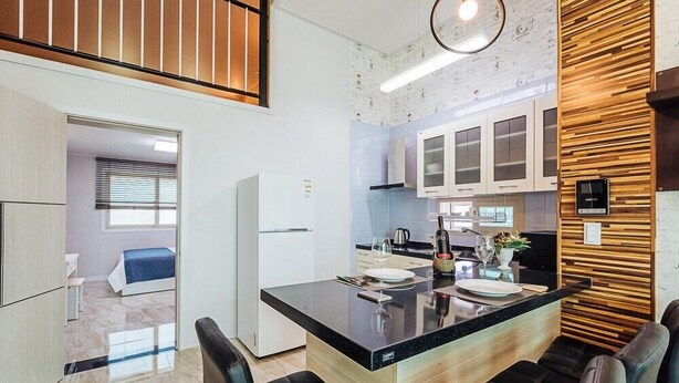 A modern kitchen with a central island, black chairs, and wooden paneling on the wall. - Maggiore Pension 1 (Pohang)