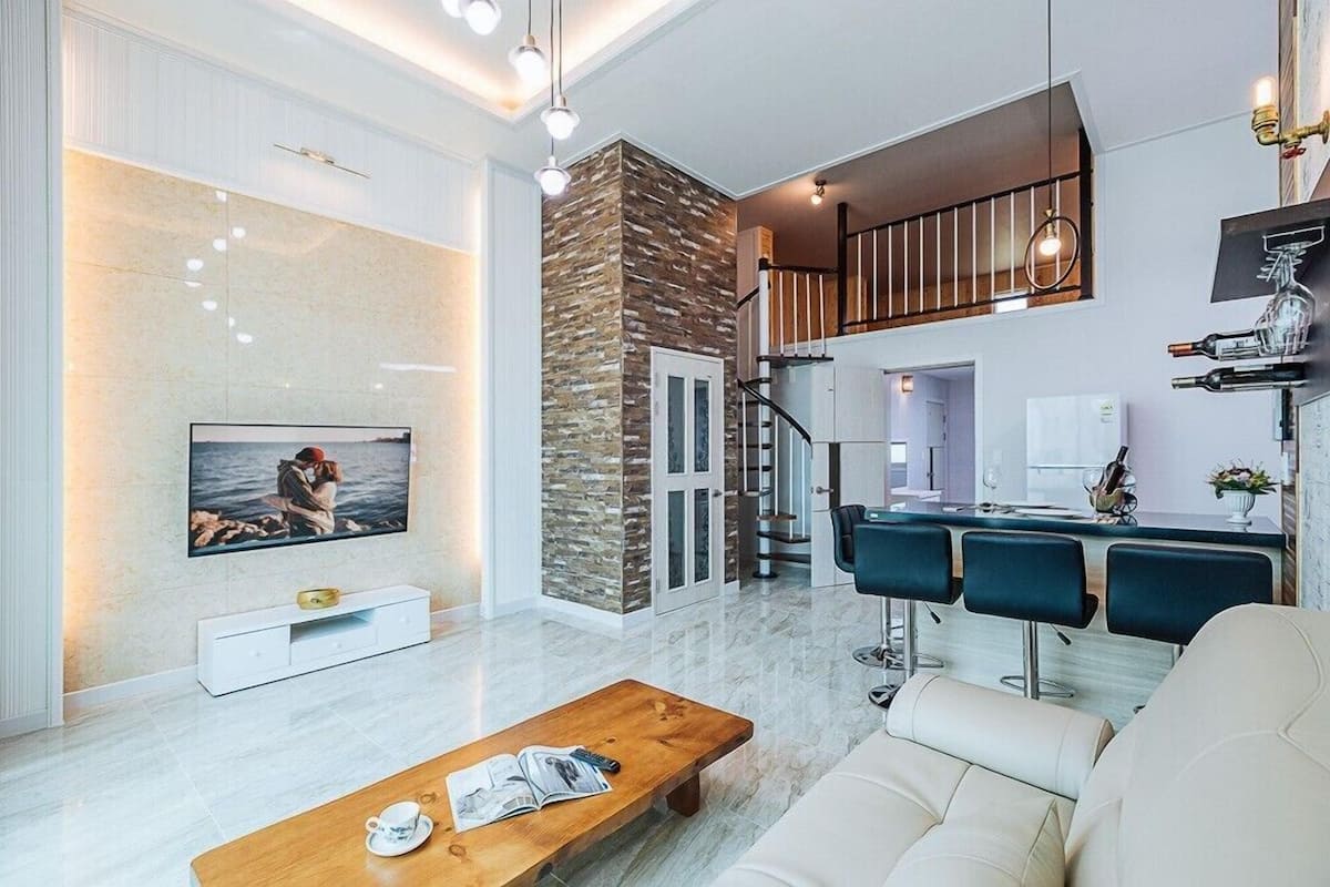 A modern living room with a TV, a wooden coffee table, a sofa, and a staircase leading to an upper level.