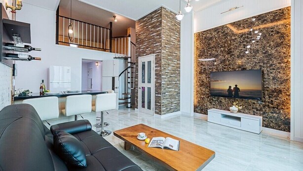 A modern living room with a black leather sofa, a wooden coffee table, and a TV on a stone-patterned wall. - Maggiore Pension 1 (Pohang)