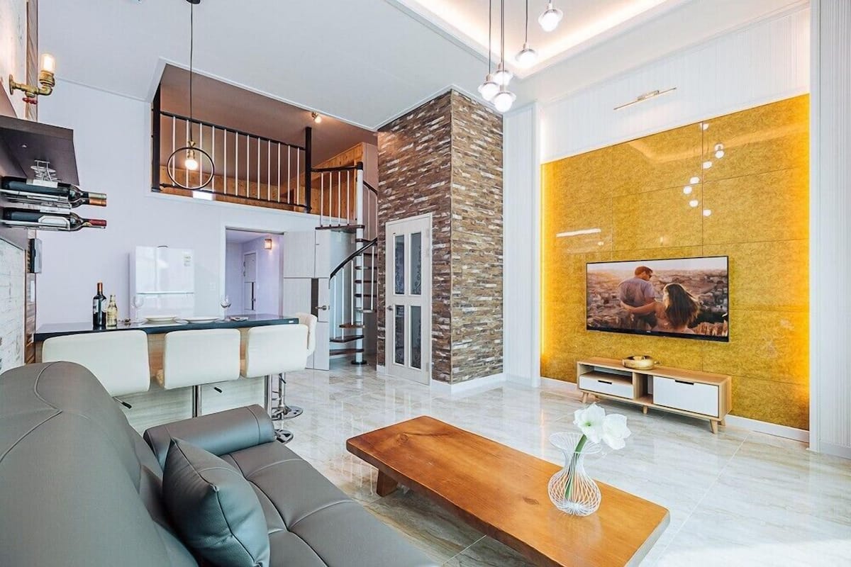 A modern living room with a sofa, coffee table, and a TV mounted on a yellow wall.