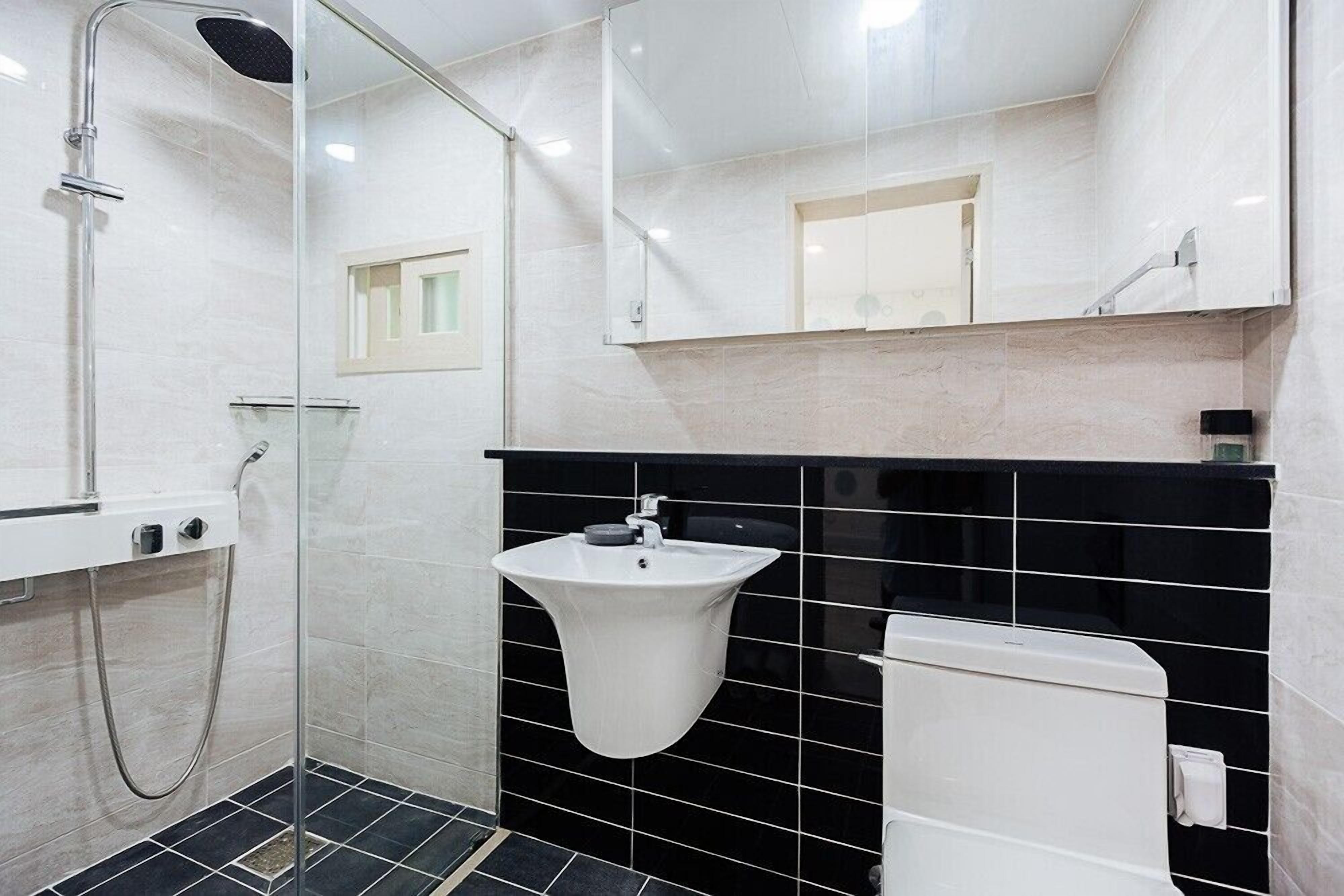 A modern bathroom with a glass-enclosed shower, a white sink, and a black tiled wall.
