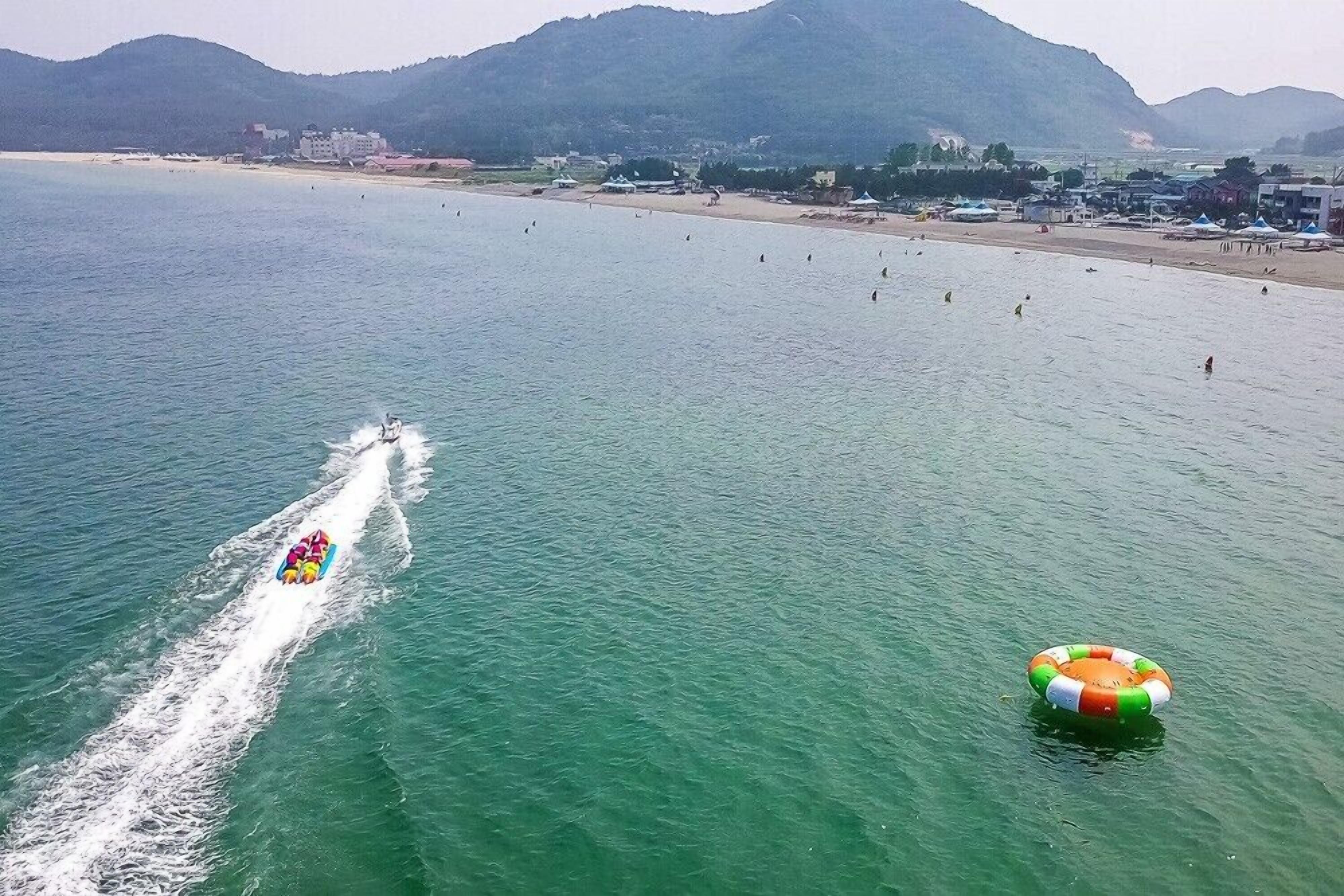 A beach with a wakeboarder and a wakeboard boat.