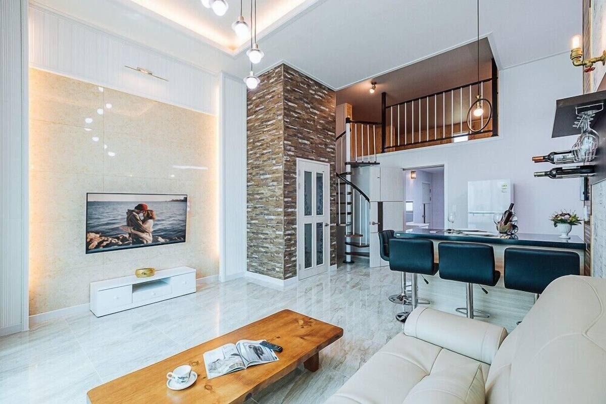 Una sala de estar moderna con televisión, una mesa de centro de madera, un sofá y una escalera que sube a un nivel superior.