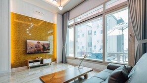 A modern living room with a large window, a flat-screen TV mounted on a textured wall, a wooden coffee table, and a leather sofa. - Majore 2 (Pohang)