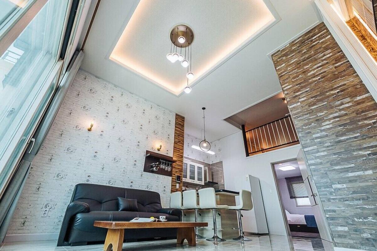 Una sala moderna con un sofá, una mesita de centro y un comedor con sillas. Se ve una cocina al fondo.