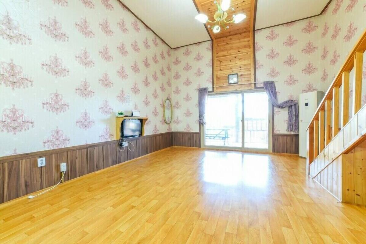 A spacious room with wooden flooring, a large window, and a wooden staircase.