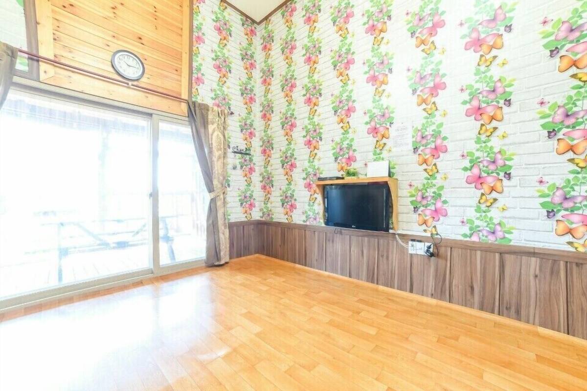 A room with a wooden floor, a brick-patterned wall with floral wallpaper, a clock, and a television on a wooden stand.