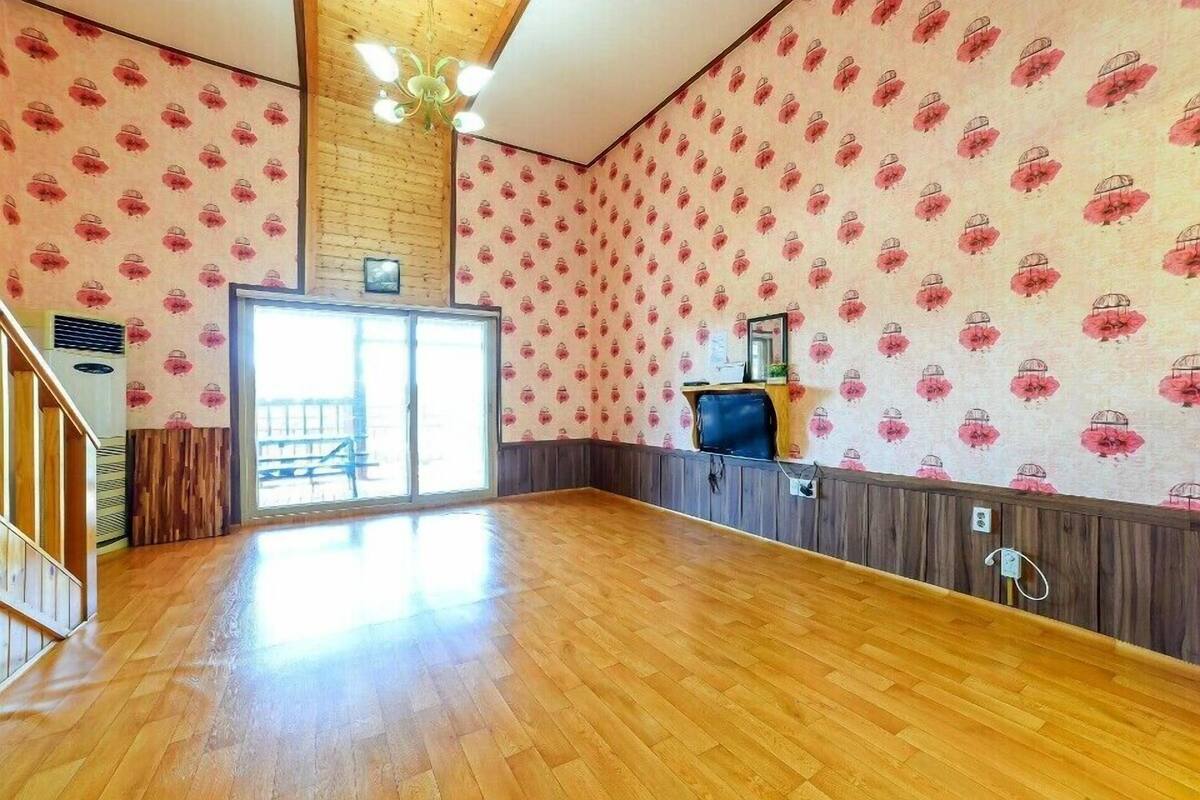 A spacious room with wooden flooring, a large window, and patterned wallpaper.