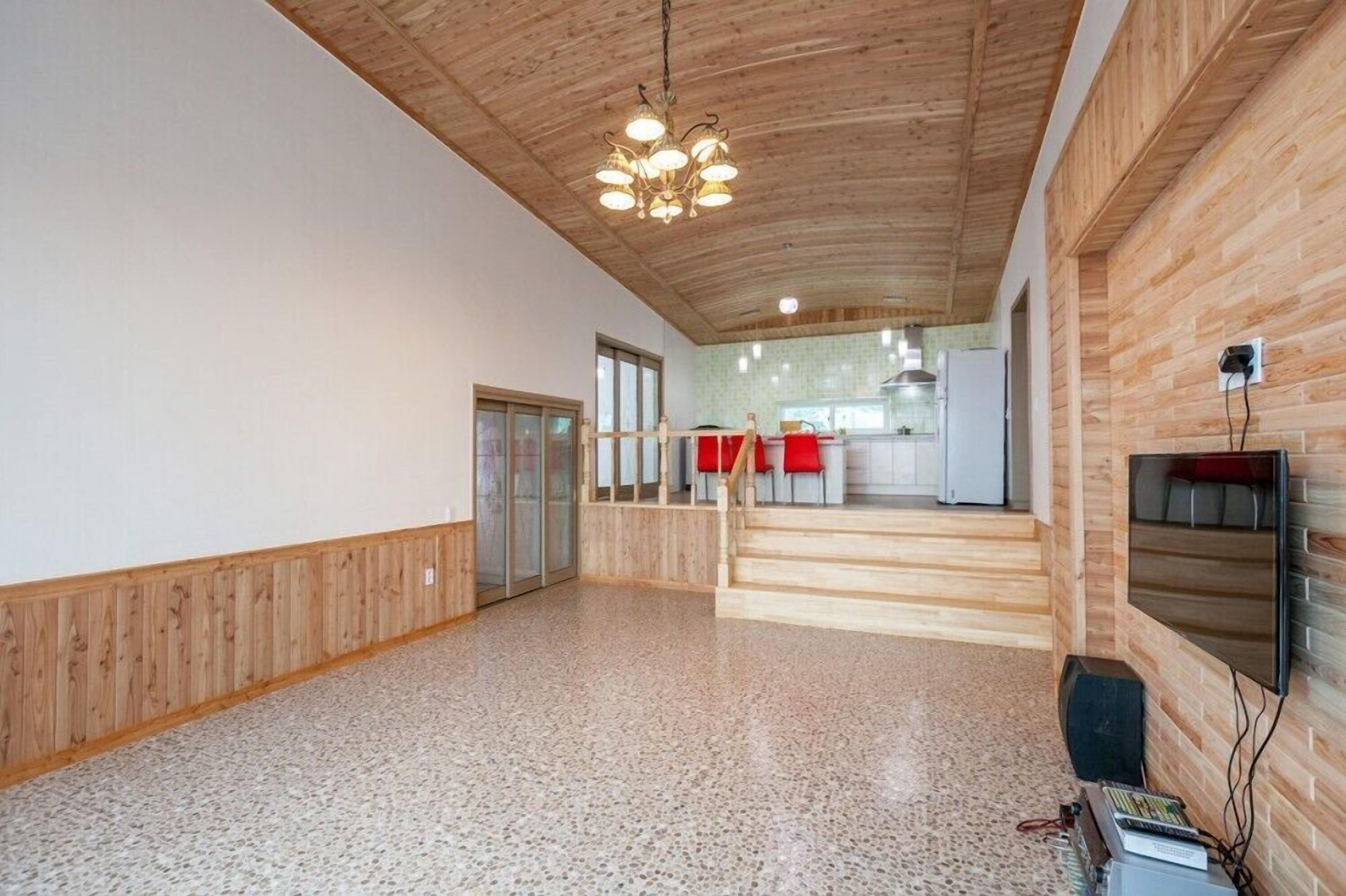 A spacious interior with a wooden ceiling, a kitchen area in the background, and a flat-screen TV mounted on the wall.