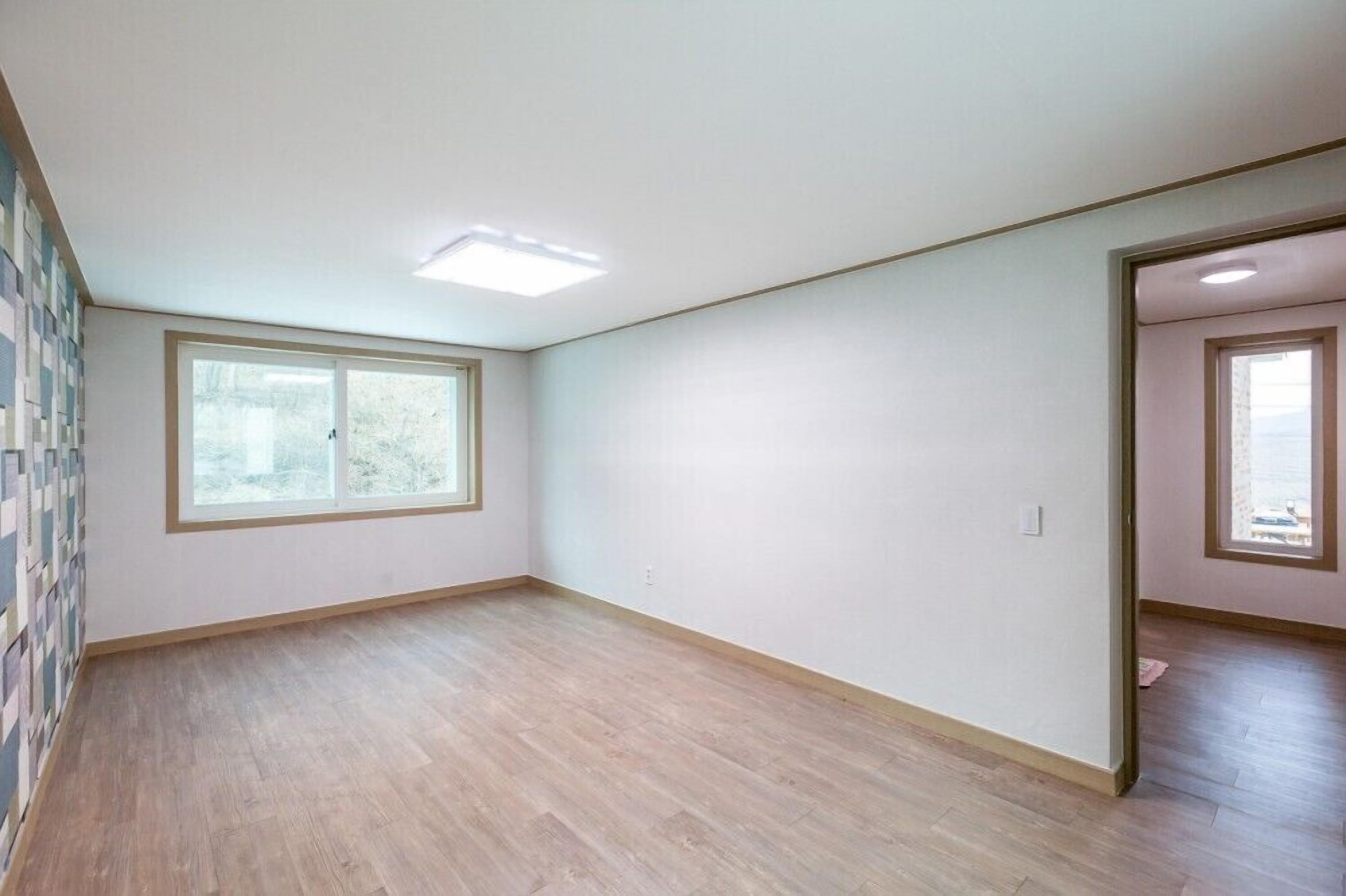 Une pièce avec un plancher en bois, une grande fenêtre et un luminaire au plafond.