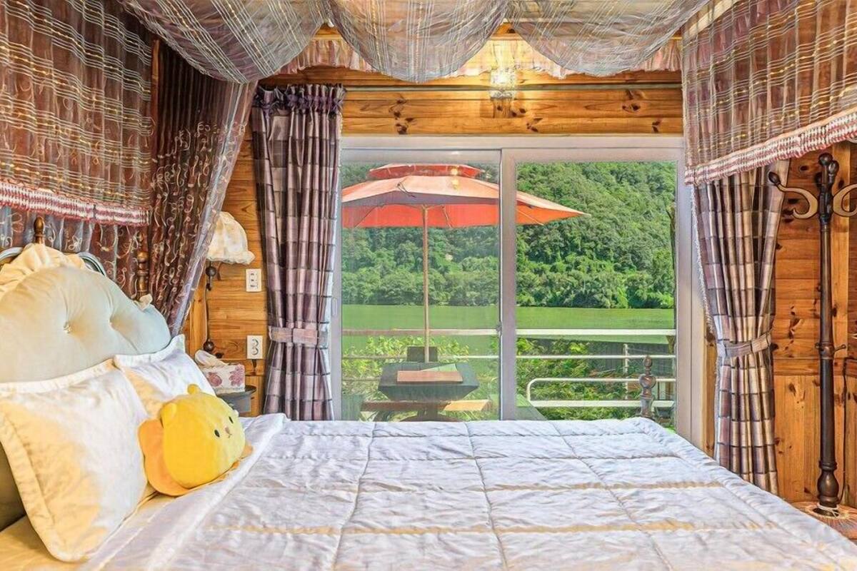A bedroom with a large bed, curtains, and a view of a garden through a sliding door.