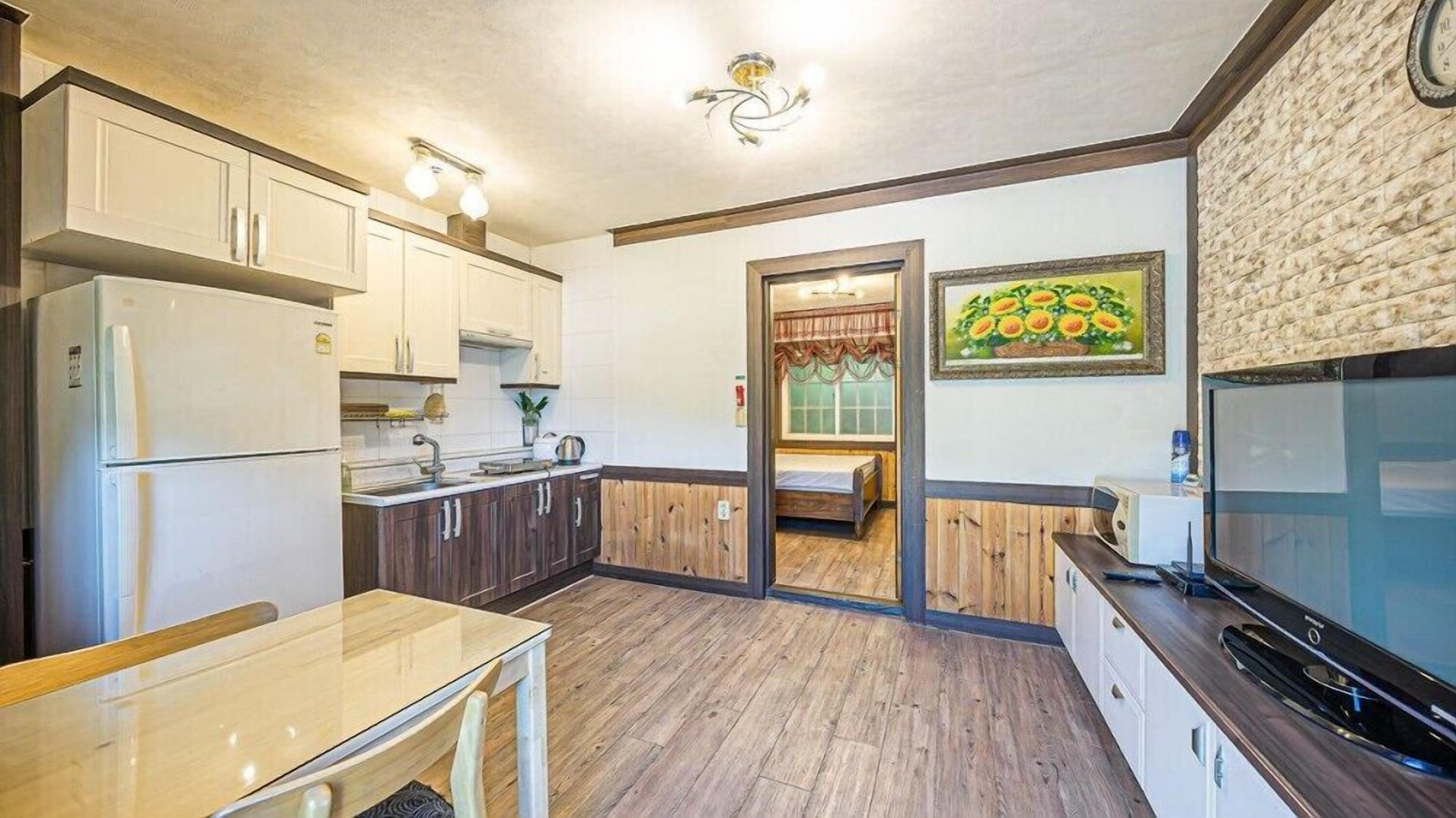 A compact kitchen with white cabinets, a wooden dining table, and a TV on the right.