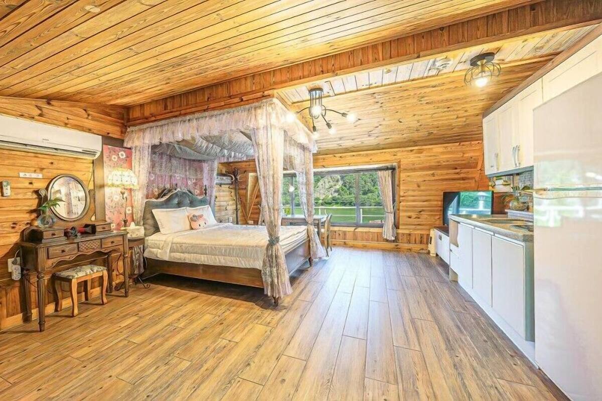 A log cabin-style room with a four-poster bed, wooden flooring, and a kitchen area with a refrigerator and sink.