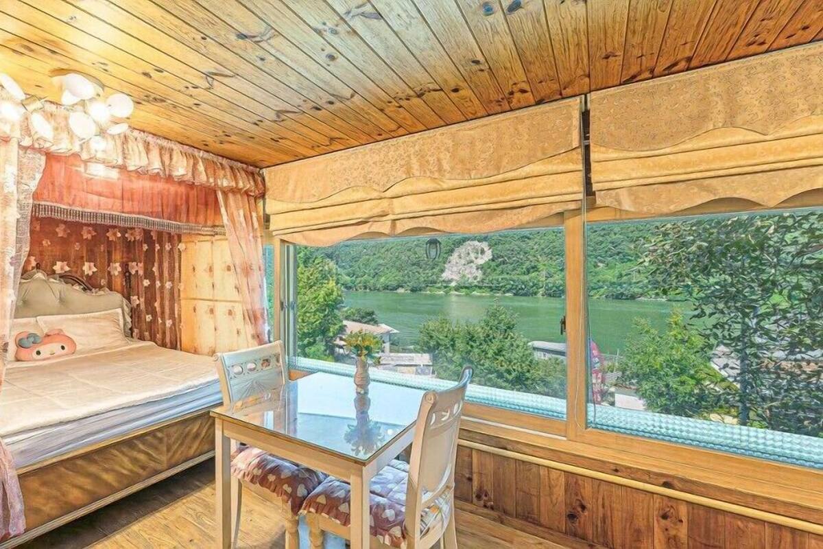 A wooden cabin room with a bed, a glass table, and a view of a lake.