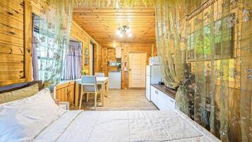 A wooden cabin interior with a bed, a small dining table, and a kitchen area.