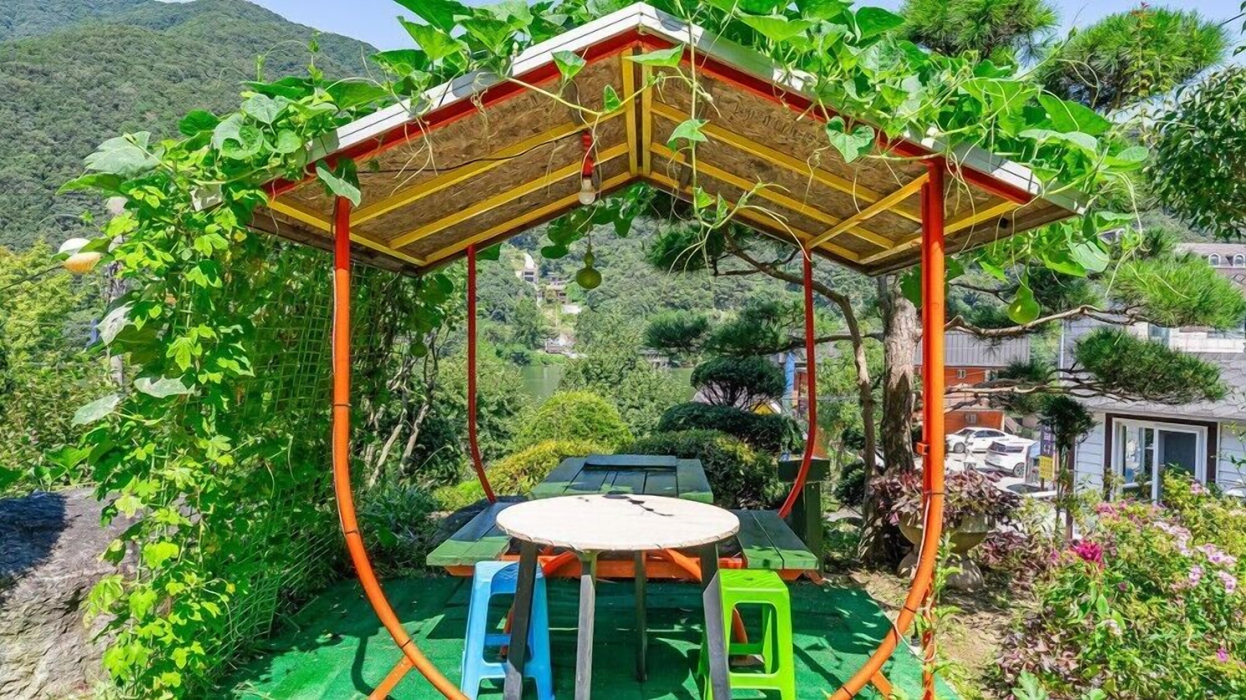 Un espace extérieur aménagé, abrité et doté de tables et de chaises, entouré d’une végétation luxuriante et offrant une vue sur un paysage montagneux.