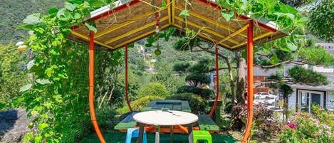 Un espace extérieur aménagé, abrité et doté de tables et de chaises, entouré d’une végétation luxuriante et offrant une vue sur un paysage montagneux.