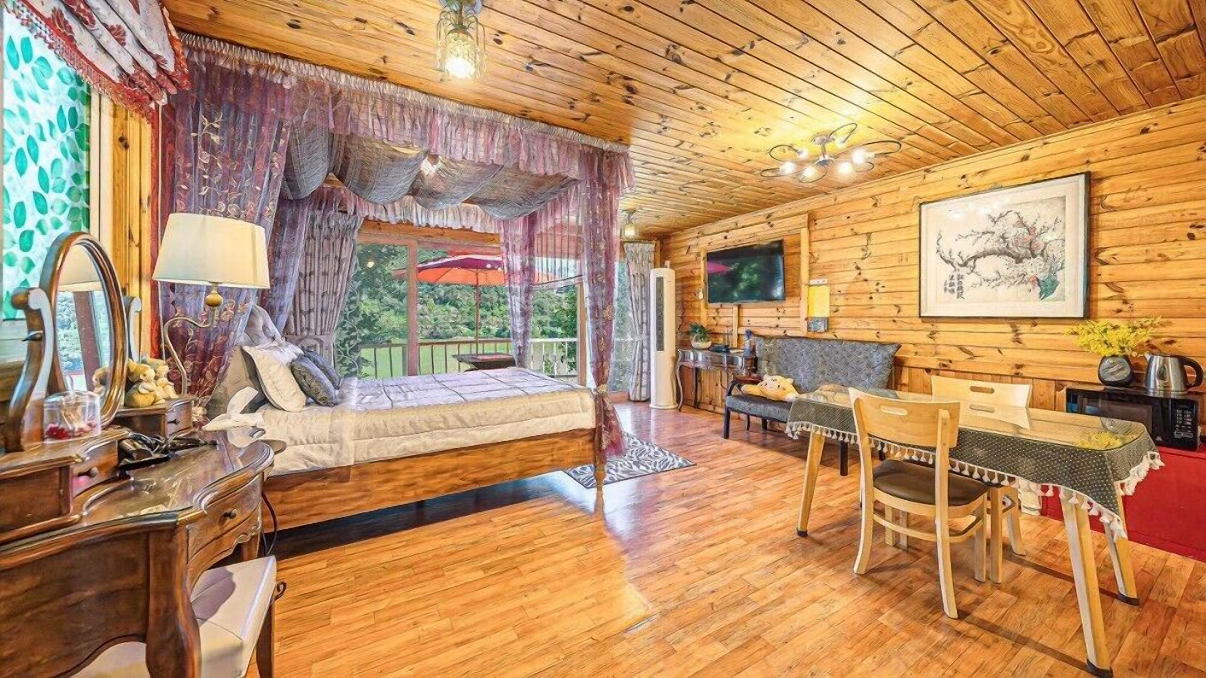 A cozy cabin-style room with a wooden floor, a bed with a canopy, a dining area with a table and chairs, and a TV mounted on the wall.