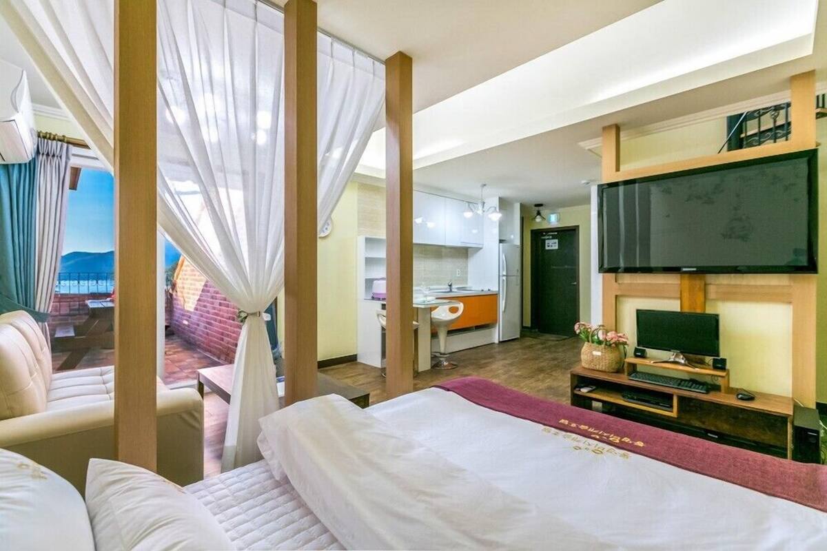 Una habitación de hotel con cama, escritorio, televisión y vistas a un balcón.