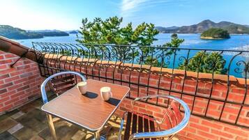 A balcony with a table and chairs, a brick wall, and a view of the sea and hills.