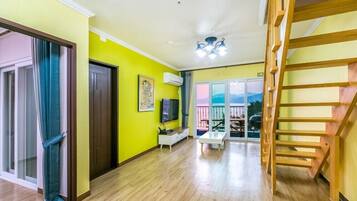 A bright living room with a wooden staircase, a TV, and a view through a glass door.