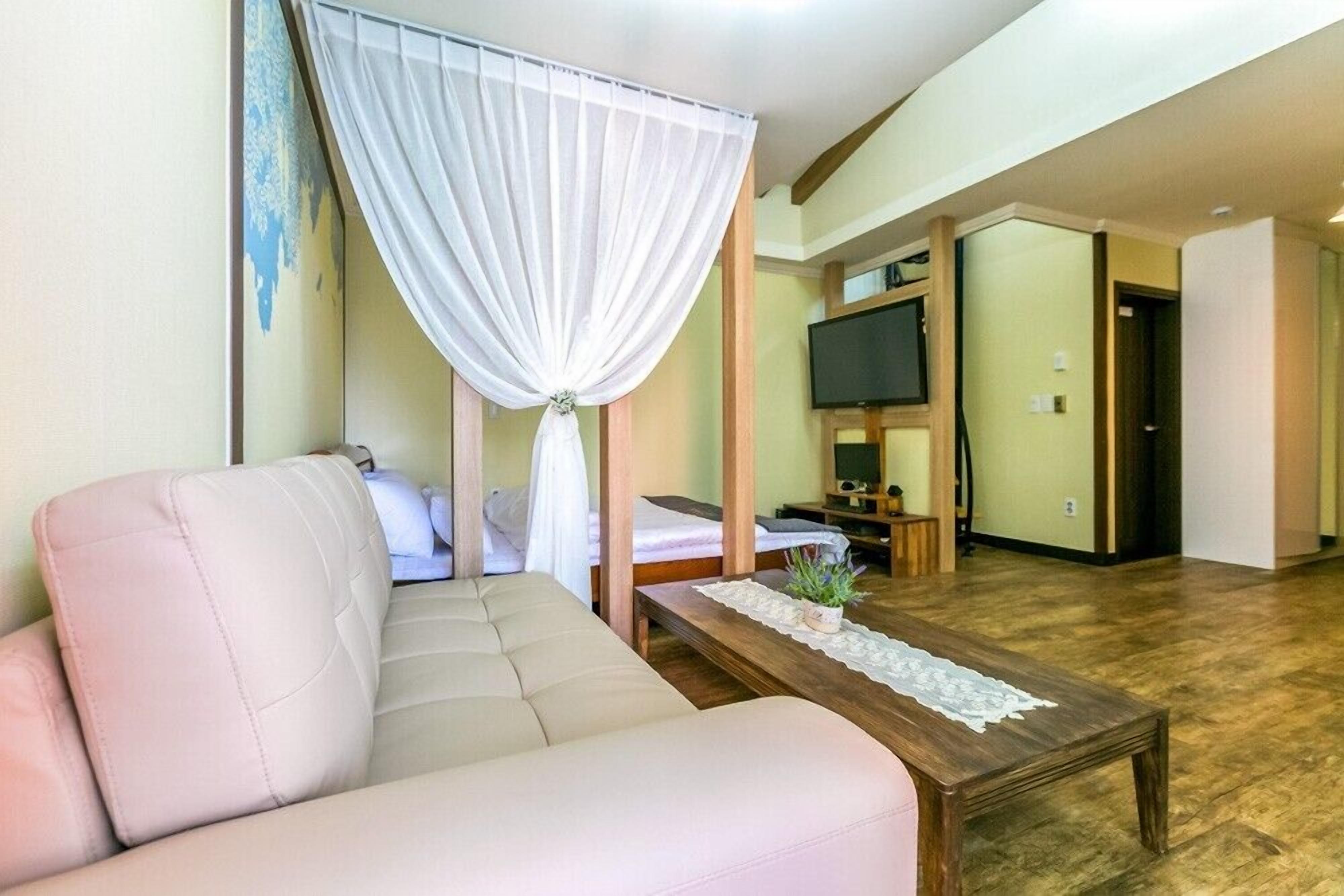 A hotel room with a sofa, a bed, a TV, and a wooden floor.