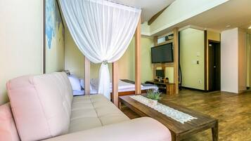 A hotel room with a sofa, a bed, a TV, and a wooden floor.