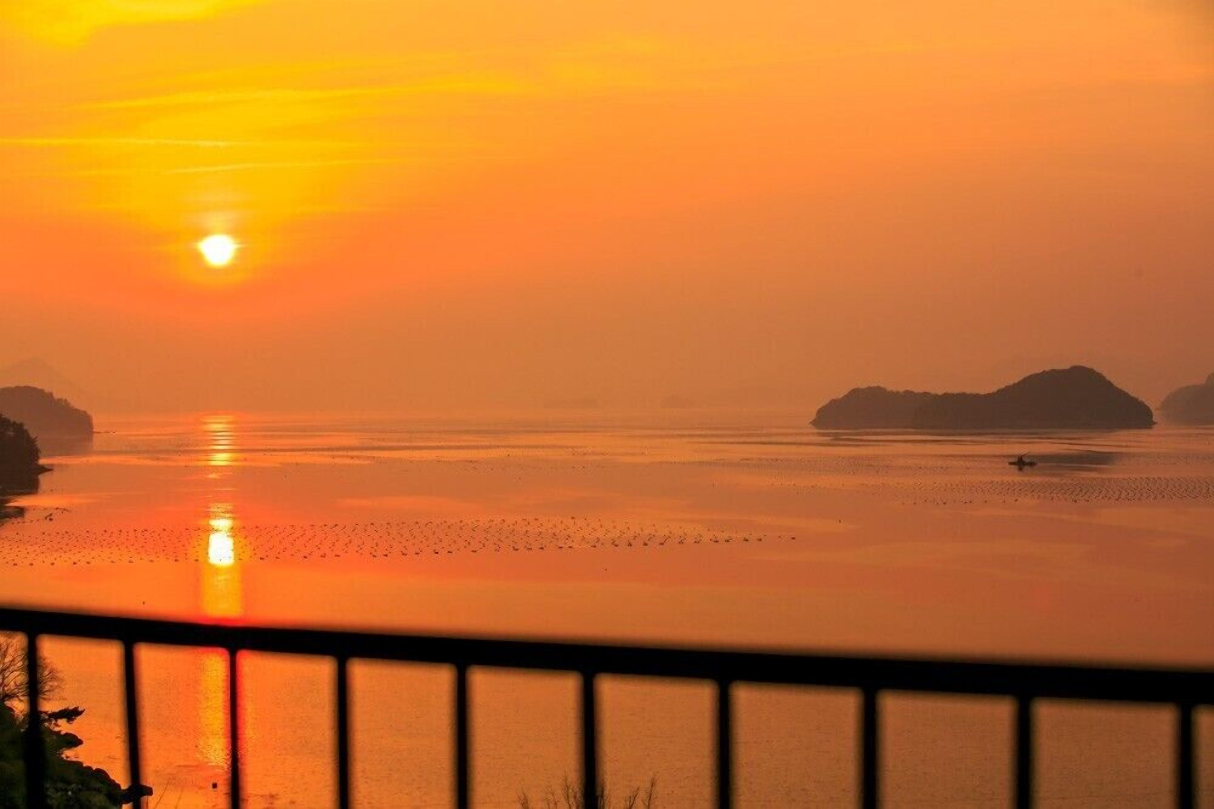 A sunset over a calm body of water with distant landforms.