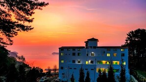 A multi-story building with a flat roof, surrounded by trees and a road with vehicles. - Beach castle hotel & resort (Tongyeong)