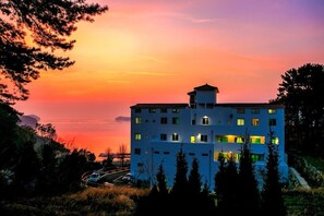 A multi-story building with a flat roof, surrounded by trees and a road with vehicles. - Beach castle hotel & resort (Tongyeong)