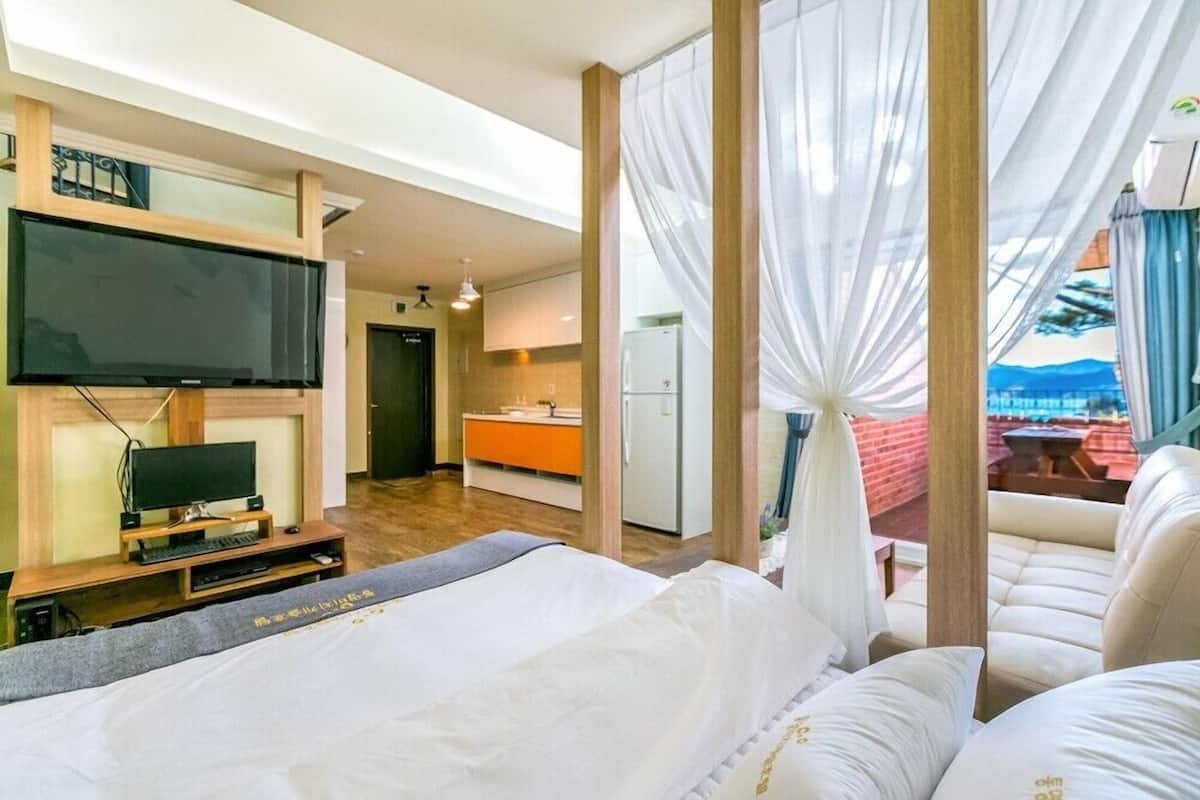 Habitación de hotel con cama, televisor, balcón con vistas y zona de comedor.