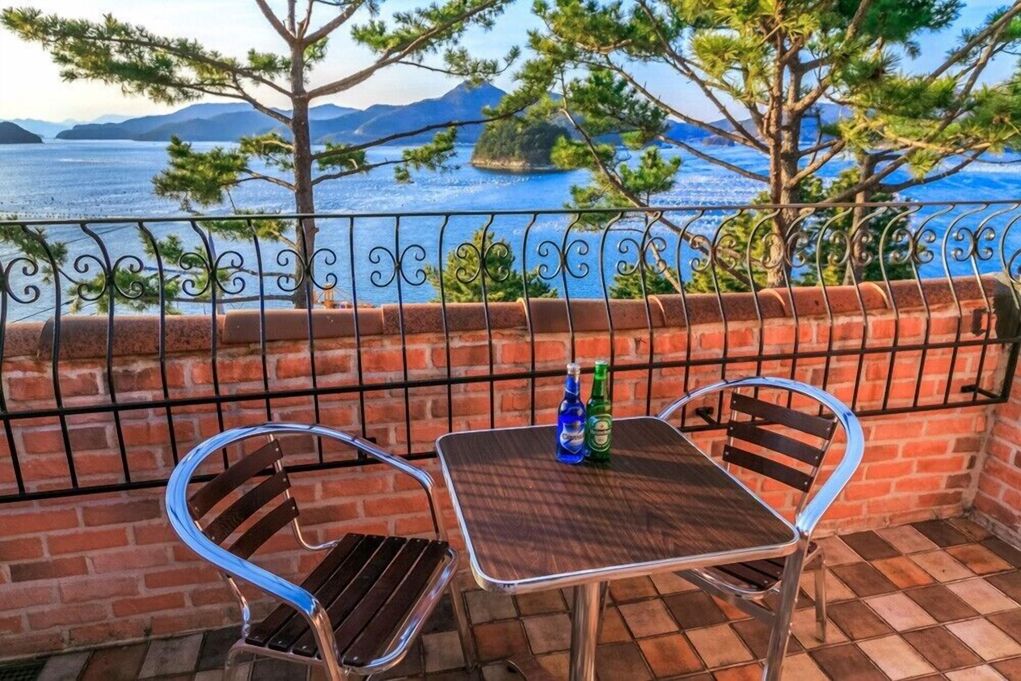 Un balcón con mesa y sillas, vista al mar y un muro de ladrillo.