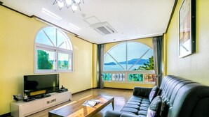 A living room with a TV, sofa, coffee table, and large windows with a view. - Beach castle hotel & resort (Tongyeong)