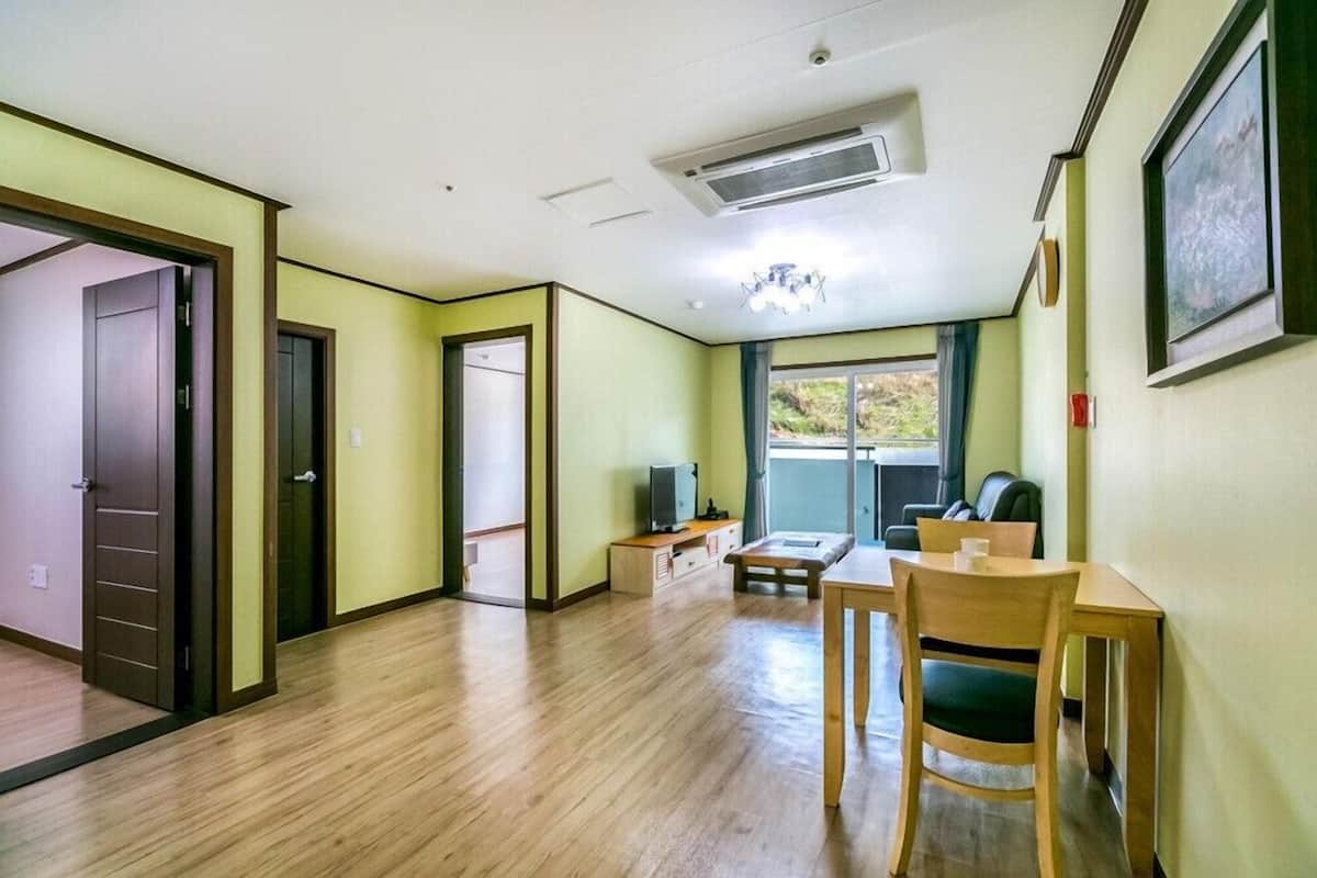 Habitación con piso de madera, un escritorio con silla, televisión y ventana con vista a vegetación.