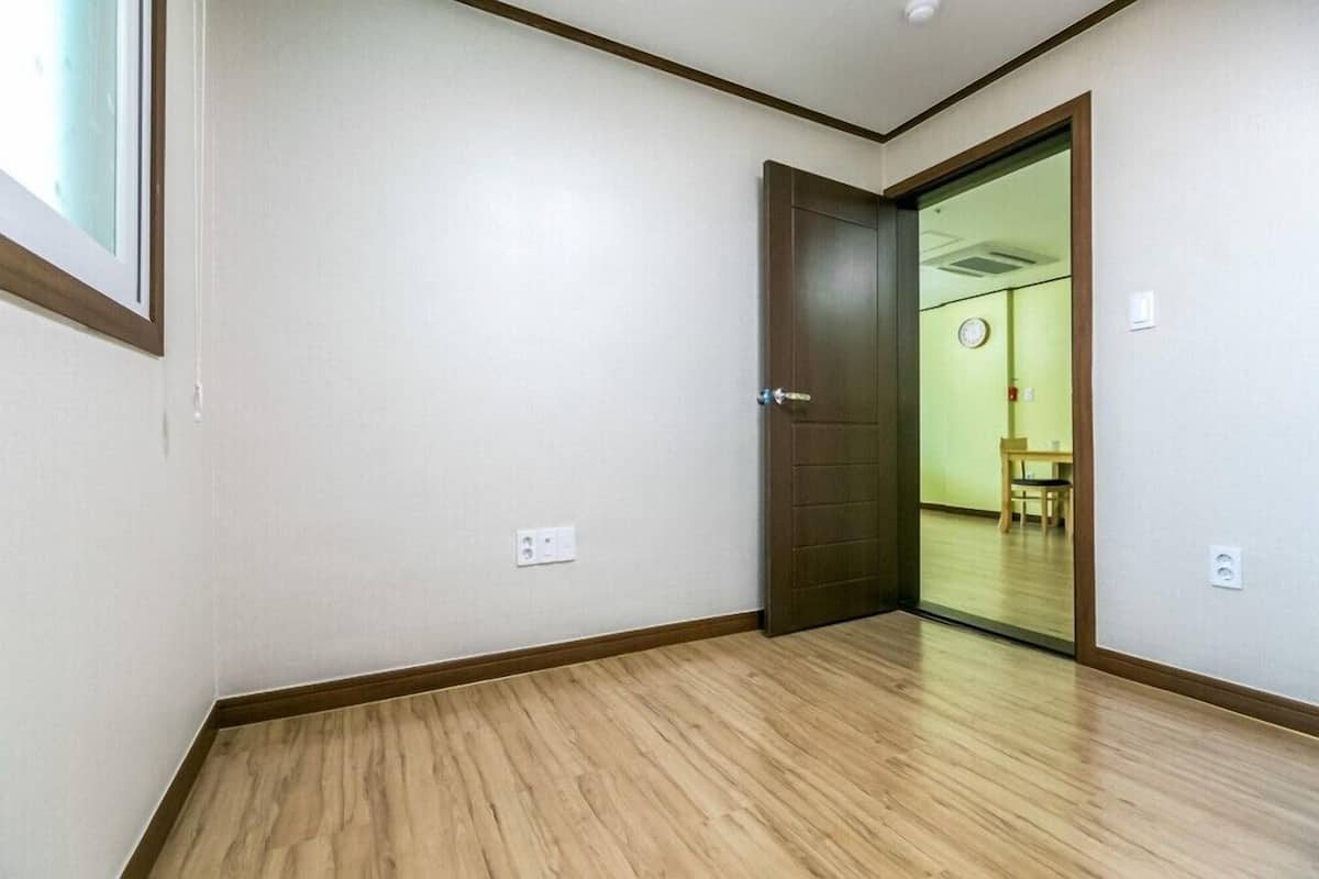 Una habitación con piso de madera, una puerta cerrada y un interruptor de luz visible en la pared.