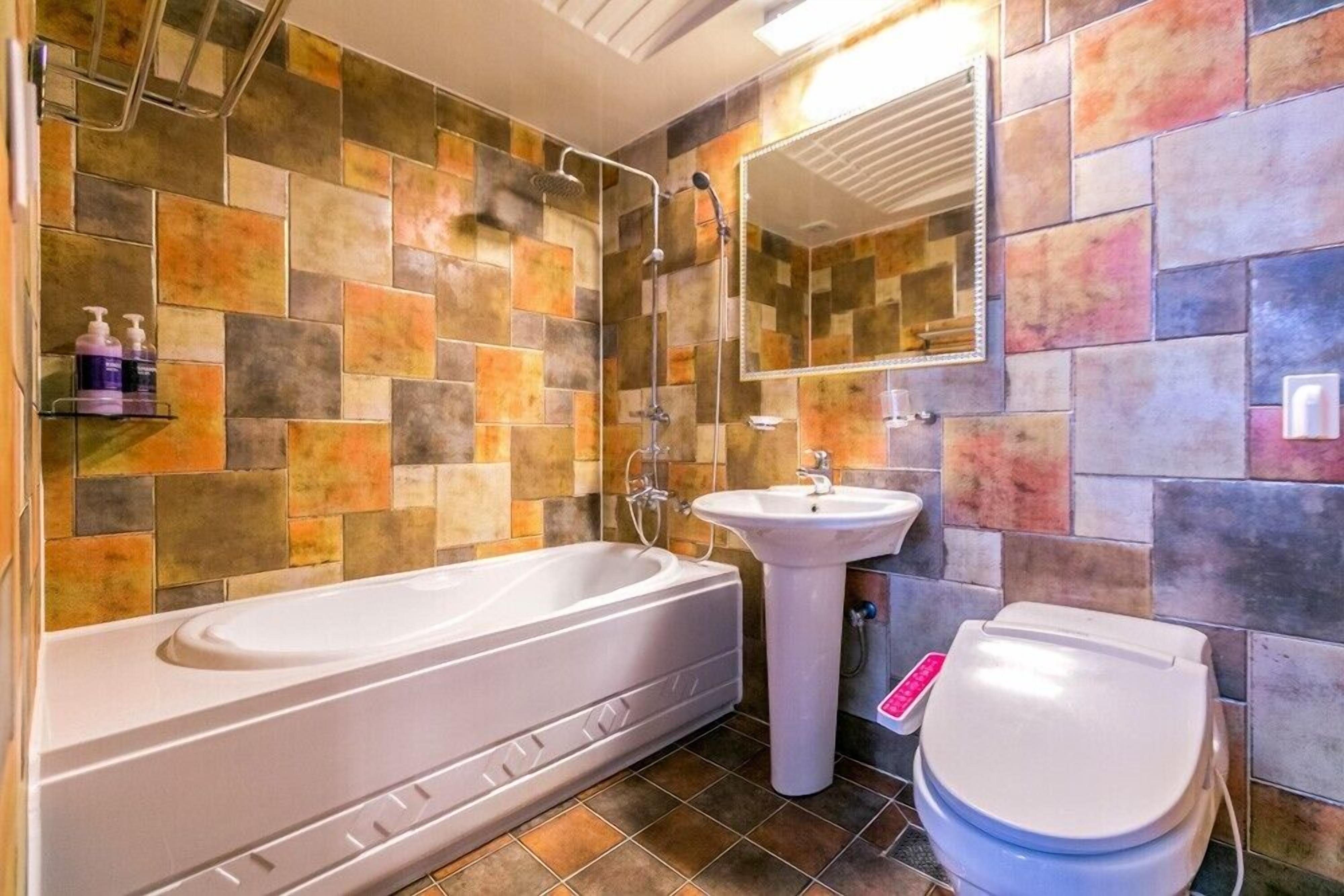 A bathroom with a bathtub, sink, and toilet, tiled with multicolored tiles.