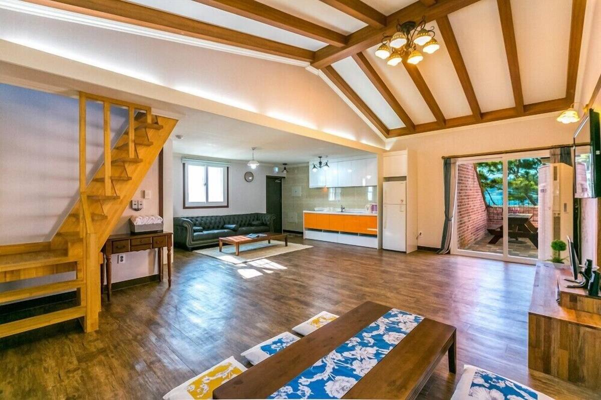 Un amplio salón con escalera de madera, un sofá, una mesa de centro y una cocina al fondo.