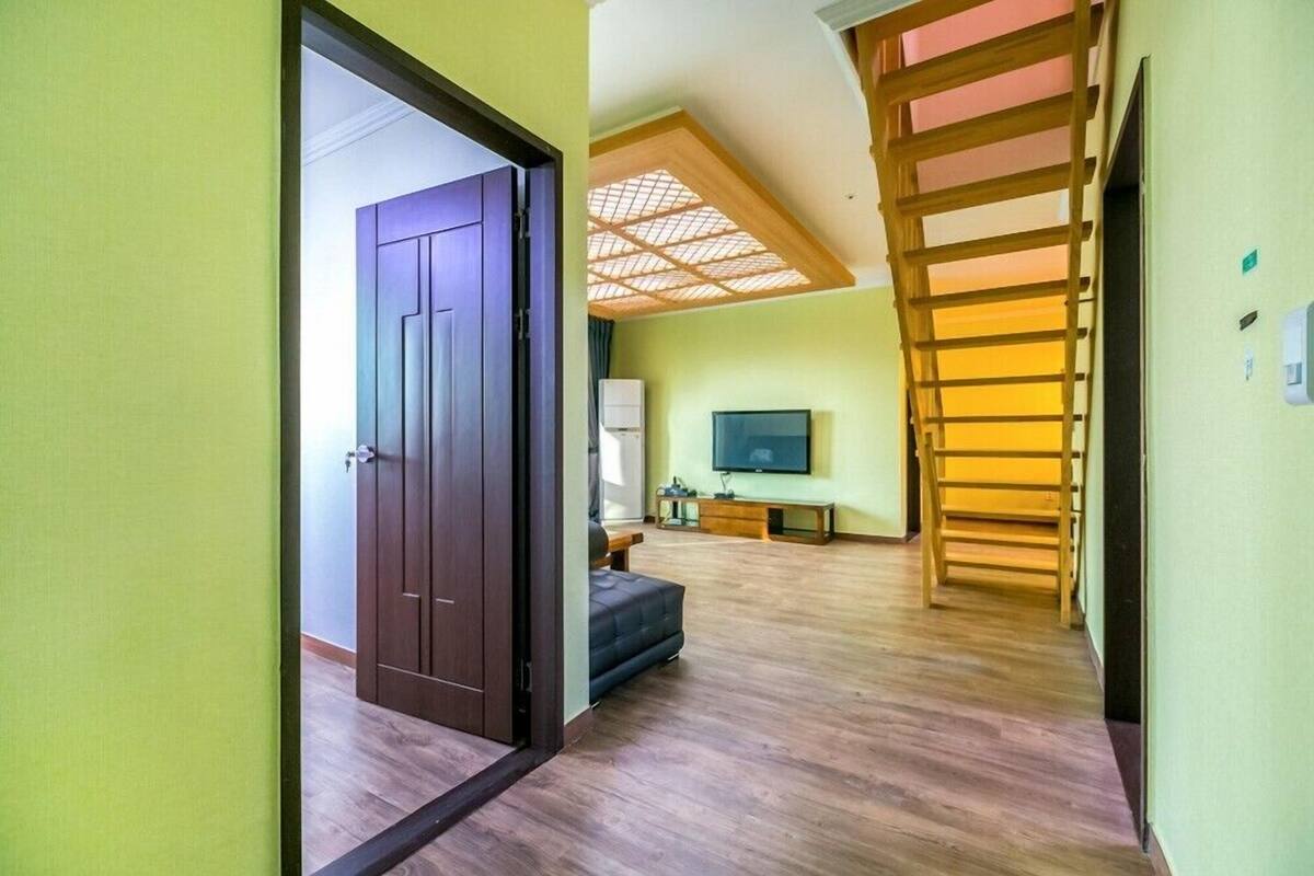 Una habitación con piso de madera, puerta oscura, televisor y una escalera.