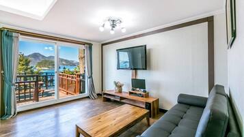 Una sala de estar con un sofá, una mesa de centro de madera, un televisor sobre un mueble bajo y un balcón con vista al mar.