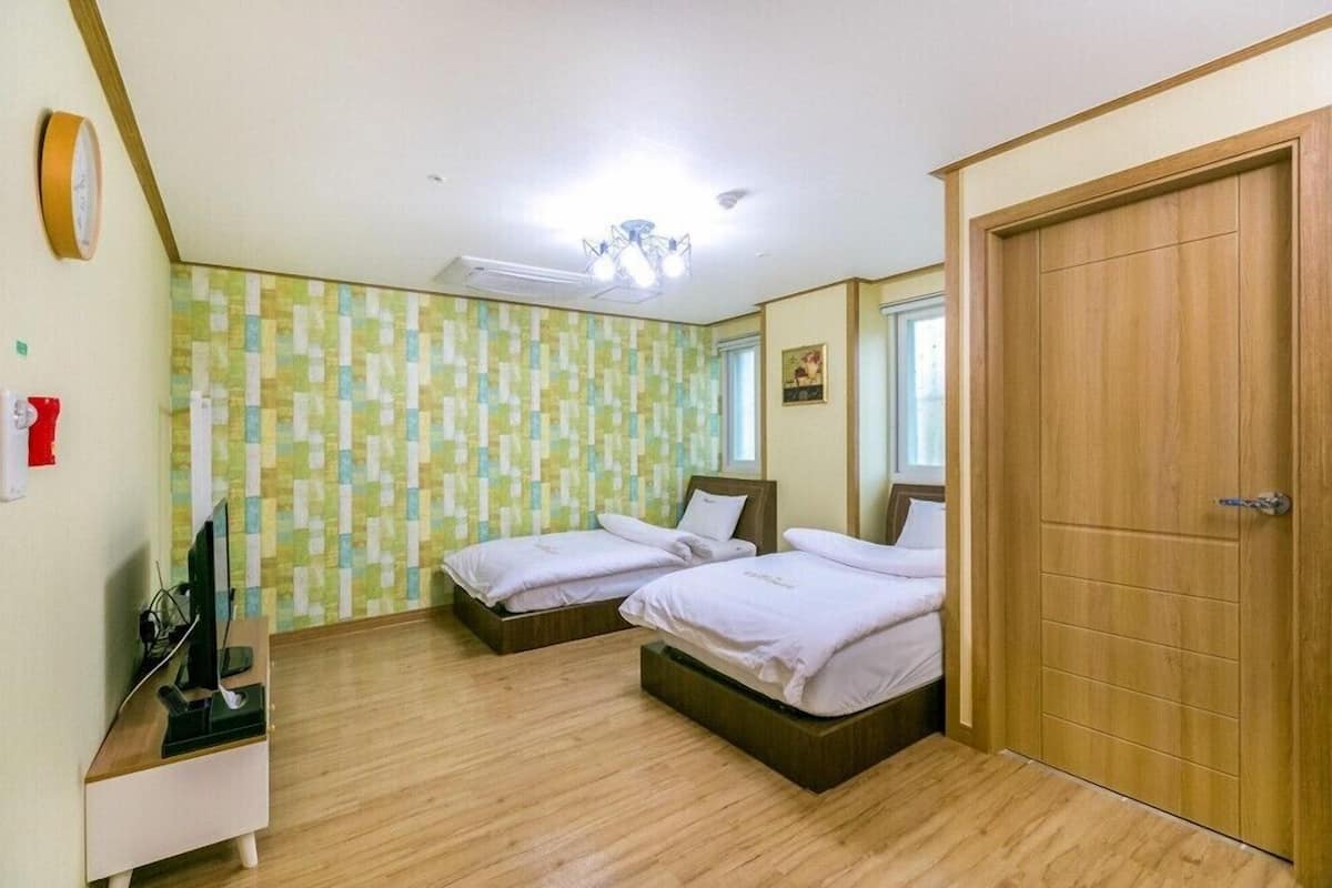 Una habitación con dos camas, un escritorio de madera, un reloj y una puerta.