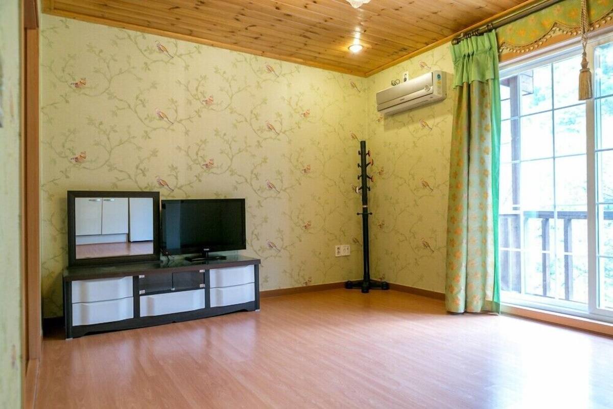 A room with a wooden ceiling, a television on a cabinet, a window with curtains, and an air conditioning unit.