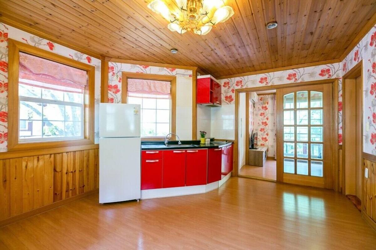 A kitchen with wooden ceiling, red cabinets, and a white refrigerator.